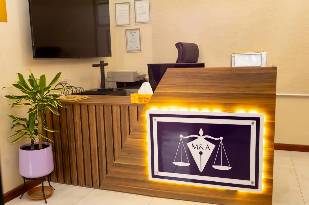 The reception desk at MacCarthy & Associates, with the firm’s scales-of-justice monogram lit behind it.